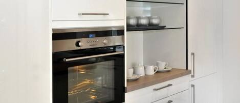 A modern kitchen with white cabinetry, a built-in oven, and a glass-fronted upper shelf.
