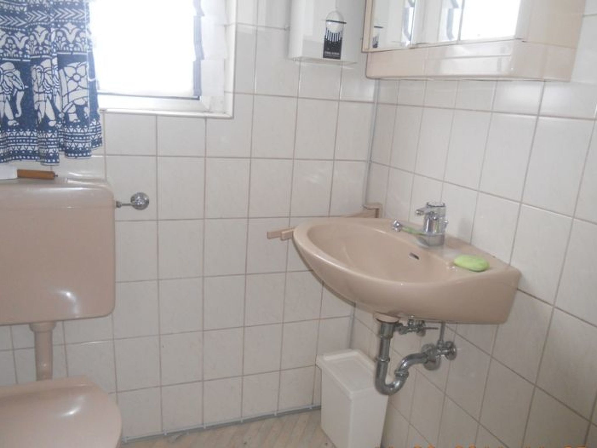 A bathroom with a toilet, sink, and a window with patterned curtains.