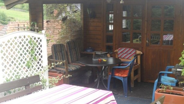 Eine überdachte Terrasse mit Tisch und Stühlen, ein Holzzaun und Blick auf die umliegende Landschaft.