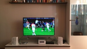 Un téléviseur à écran plat posé sur une étagère en verre, avec une collection de livres au-dessus et un vase sur la droite.