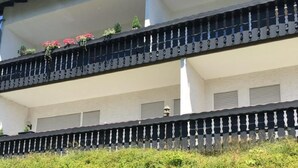 Un immeuble à plusieurs étages doté de balcons, d’un panneau indiquant un parking et d’une haie verte.