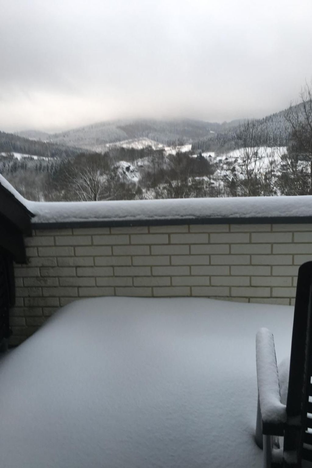 A snow-covered patio with a brick wall and a view of a snowy landscape.