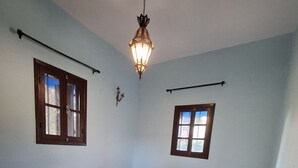 Een slaapkamer met een bed, een kamerkleed met patroon, een hanglamp en twee ramen.
