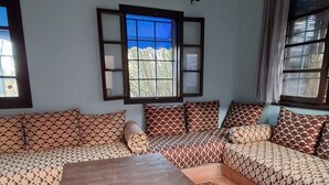 Een woonkamer met een zithoek, een houten salontafel, vloerkleden met een patroon en een raam met uitzicht op bergen.