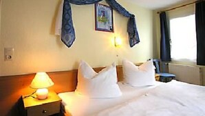 Een hotelkamer met een bed, een nachtkastje met een lamp, een lijst met een foto aan de muur, en een raam met gordijnen.