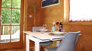 A wooden cabin interior with a dining table set for two, a framed picture on the wall, and a window overlooking greenery. - Studio Blockhaus by Interhome (Bernau)