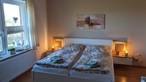 Een slaapkamer met een bed, bedlampjes, een raam met gordijnen en een schilderij aan de muur.