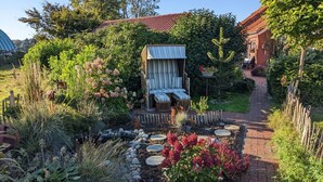 Een tuin met een houten bankje, een tuinhuisje en een pad van baksteen.