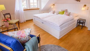Un dormitorio con una cama grande, una mesita, una silla y una ventana con cortinas.