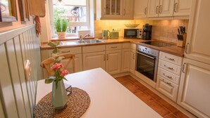 Una cocina con armarios blancos, microondas, cafetera y lavamanos.