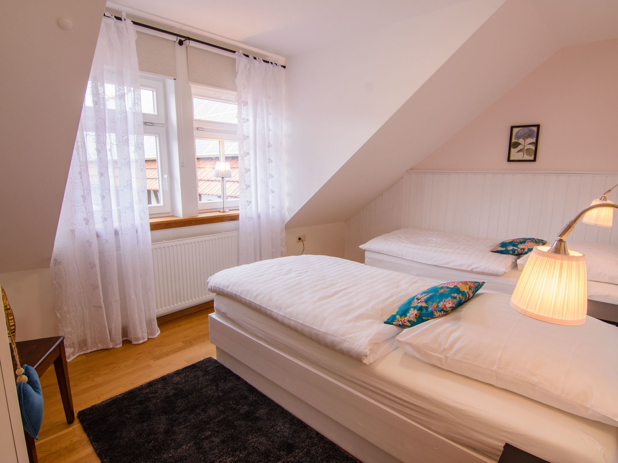 A bedroom with two beds, a window with sheer curtains, a bedside lamp, and a black rug.