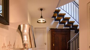 Un pasillo con una escalera, una puerta, una planta en maceta, una lámpara y un tapete.