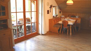 Uma área de jantar acolhedora, com mobiliário de madeira, uma janela grande com cortinas e teto de madeira.