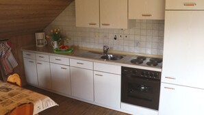 Uma cozinha compacta com armários brancos, máquina de lavar louça embutida, fogão e pia.
