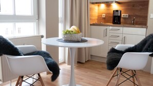Une cuisine moderne avec des meubles blancs, une machine à café et un panier de fruits posé sur une table blanche.