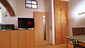 Een kleine keuken met houten kastjes, een magnetron en een flatscreen televisie.