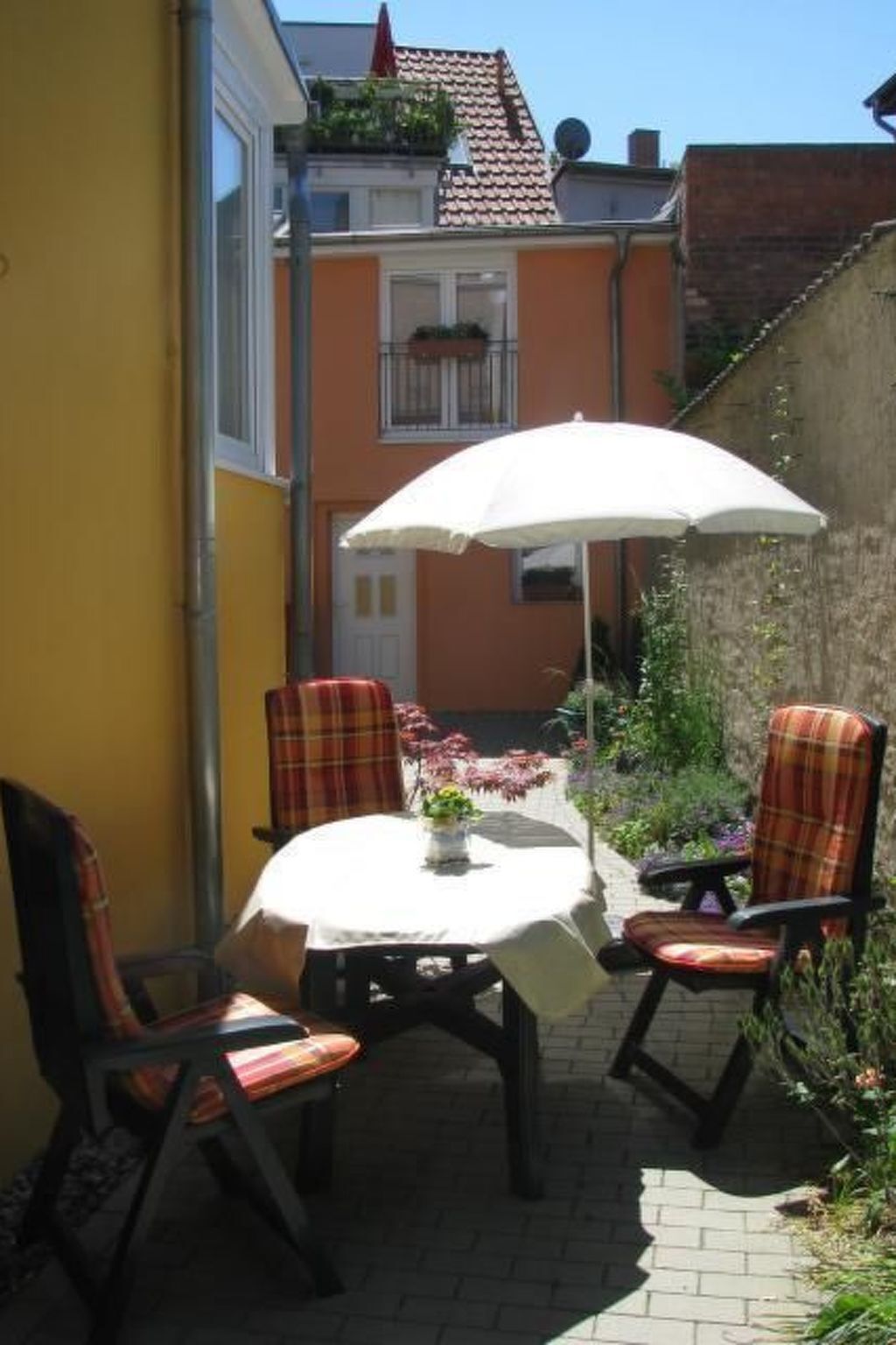 Une terrasse extérieure avec une table et des chaises, un parasol et un bâtiment jaune en arrière-plan.