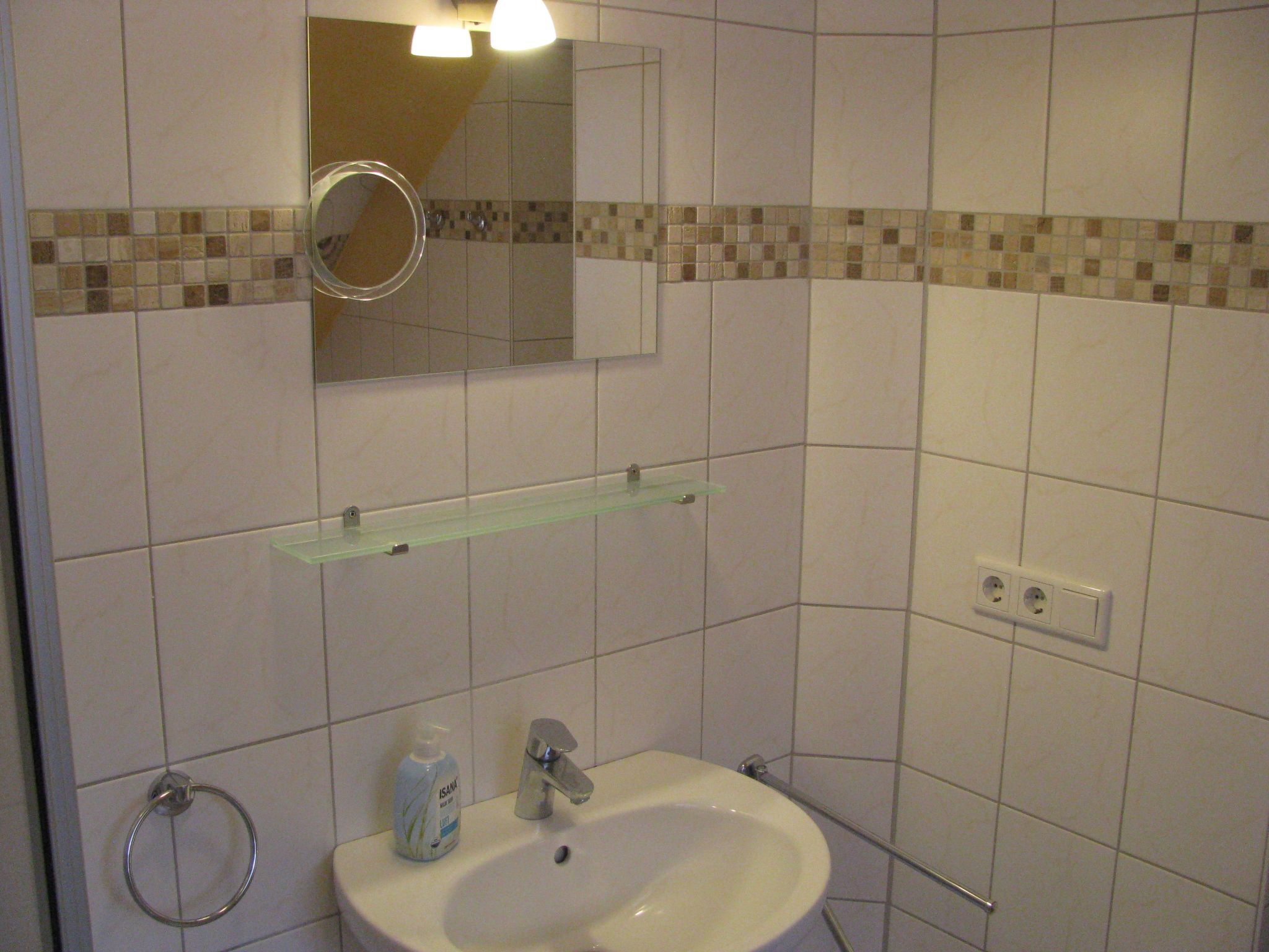 Un baño con lavamanos, espejo y dos repisas.