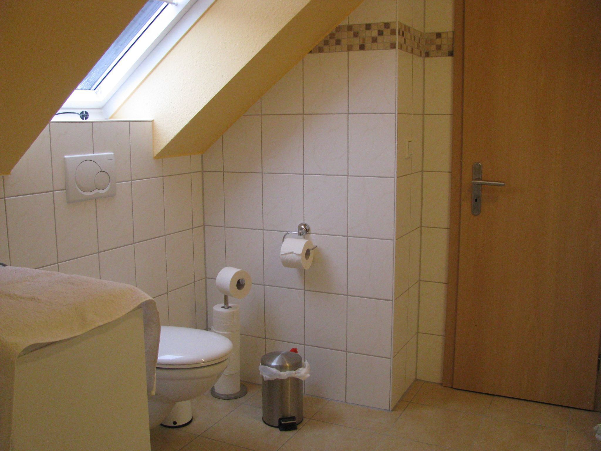 Une petite salle de bain avec des toilettes, une poubelle et un rouleau de papier toilette accroché au mur.