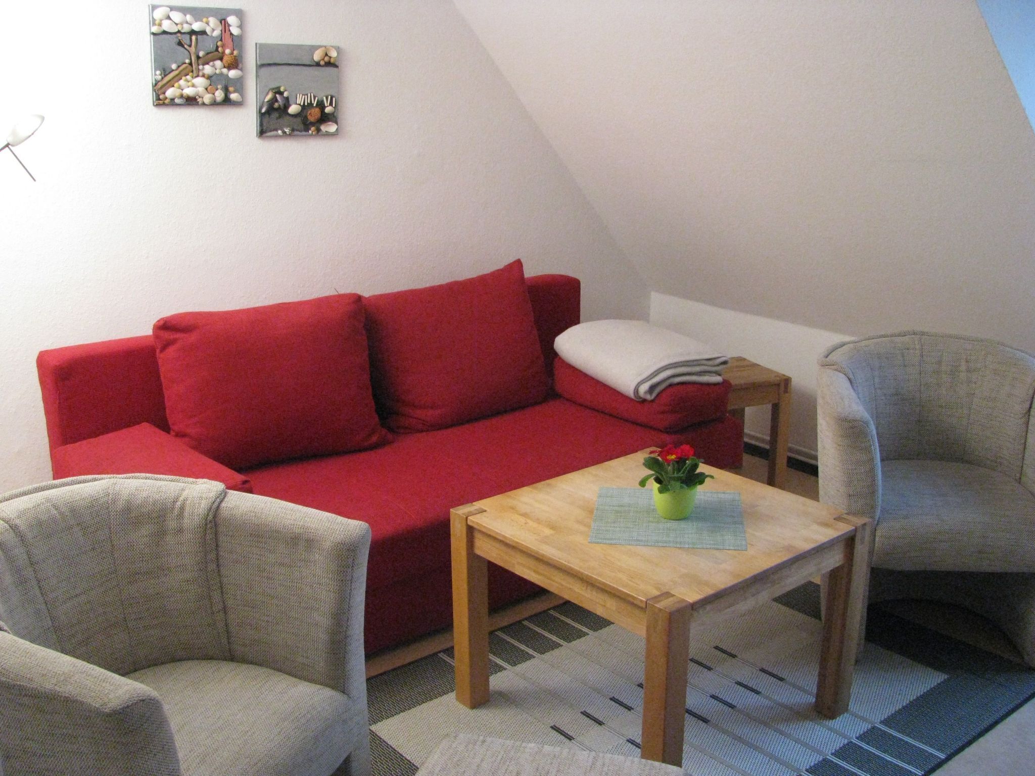 Een rode bank, twee fauteuils, een houten bijzettafeltje en een kleine groene plant.