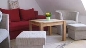 A cozy living room with a red sofa, grey armchairs, a wooden coffee table, and a small potted plant. - Moderne Ferienwohnung mitten in Greifswald by Interhome (Greifswald)