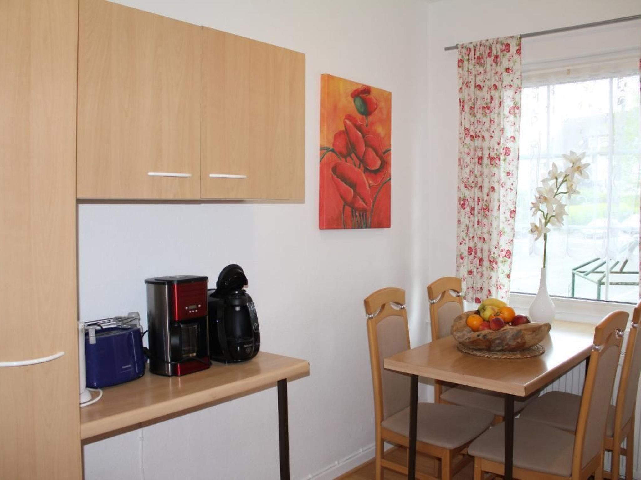 A small kitchen with wooden cabinets, a coffee maker, a toaster, and a fruit bowl on the table.
