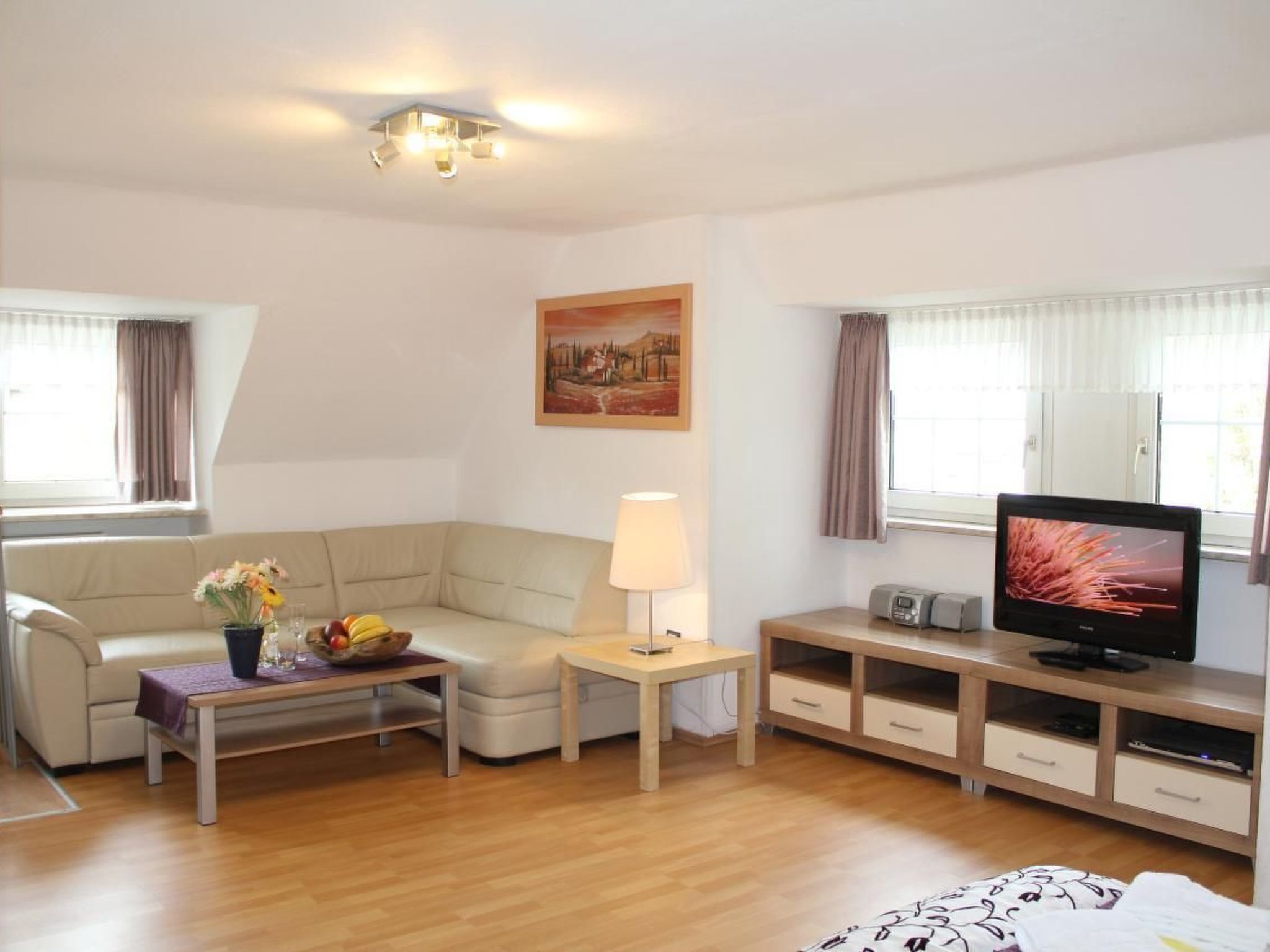 A modern living room with a sofa, a coffee table with fruit, a lamp, a TV, and a painting on the wall.