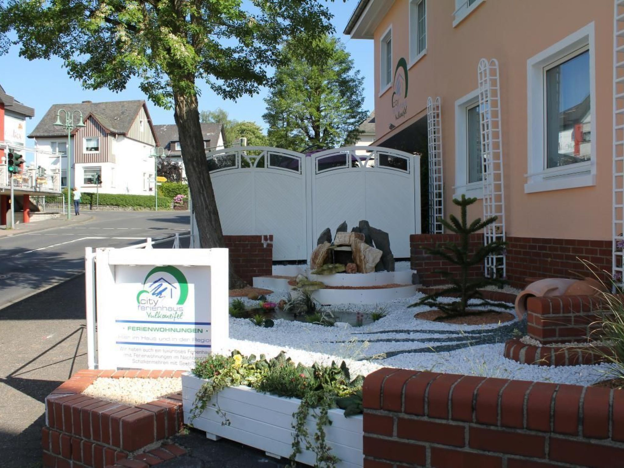 Ein Wohngebäude mit einem verschlossenen Eingang, einem kleinen Garten mit Feuerstelle und einem Schild, das es als 'City Ferienhaus' bezeichnet.