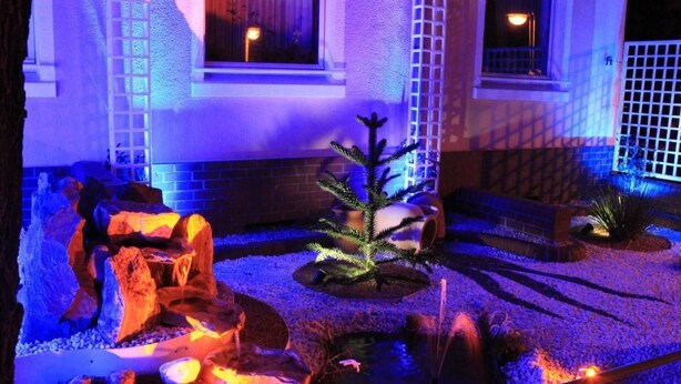A landscaped garden with a rock formation, a small tree, and a water feature in front of a building with windows and a door. - Schöne Ferienwohnung in Daun mit Garten by Interhome (Daun)