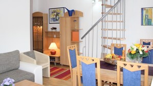 A modern living room with a wooden dining table, chairs, a sofa, a lamp, and a staircase with a metal railing. - Schöne Ferienwohnung in Daun mit Garten by Interhome (Daun)