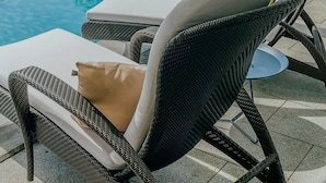 Ett område vid poolen med flätade solstolar och utsikt över det omgivande landskapet.