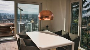 Ett modernt matområde med ett vitt bord och mörka stolar, stora fönster som ger utsikt över en byggarbetsplats och avlägsna berg.