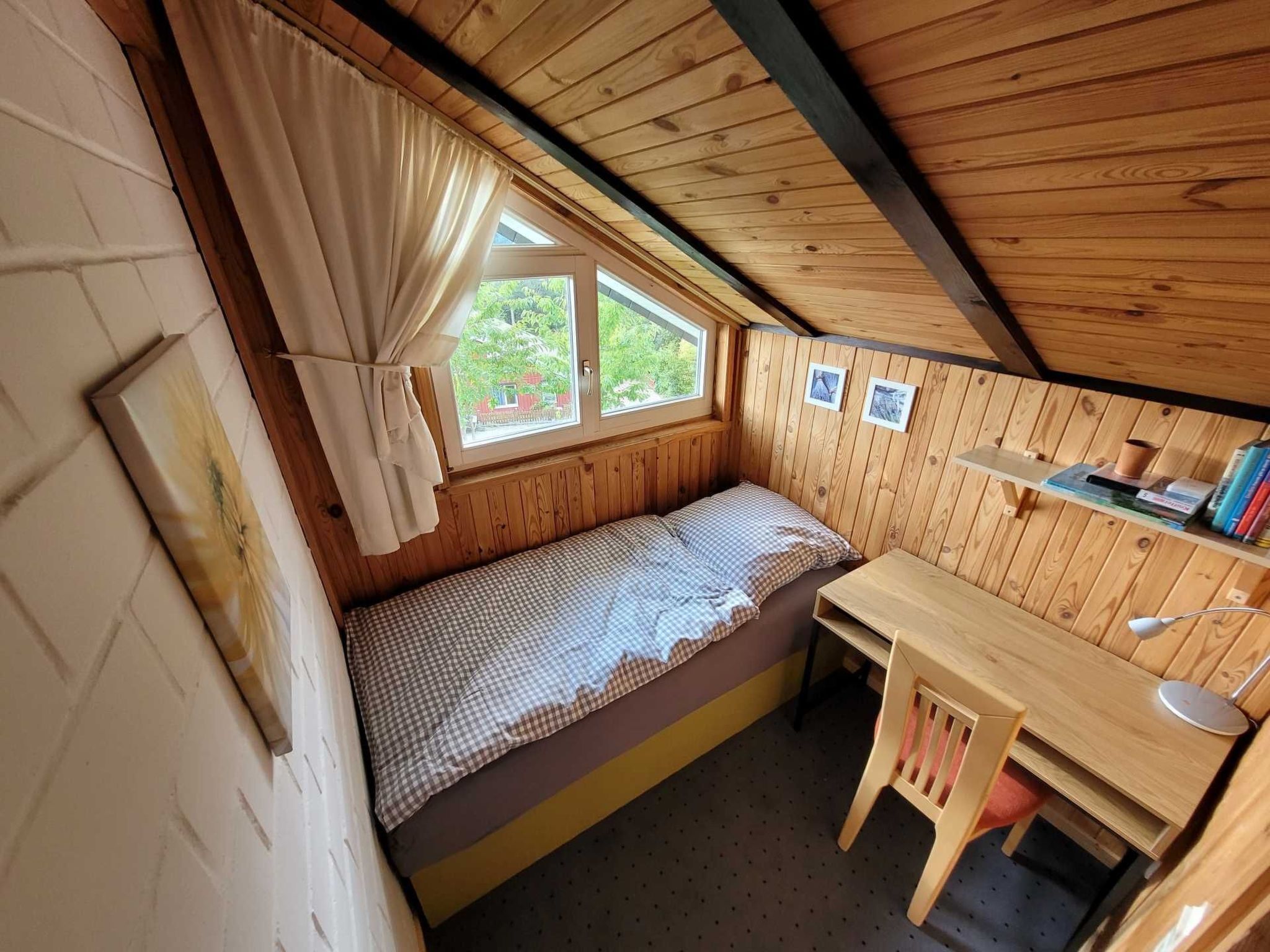 A cozy room with a bed, a small desk, and a window.