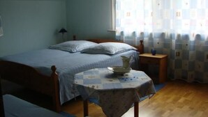 Ein Schlafzimmer mit einem Bett, einem kleinen Tisch mit kariertem Tischläufer und einem Fenster mit gemusterten Vorhängen.