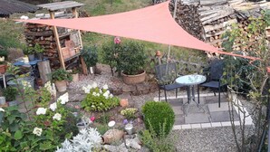 Un espace patio aménagé dans le jardin, avec une table et des chaises, entouré de différents pots de plantes et d’une pile de bois de chauffage.