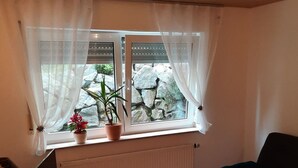 Une pièce avec une fenêtre, un radiateur, un plancher en bois et un canapé noir.