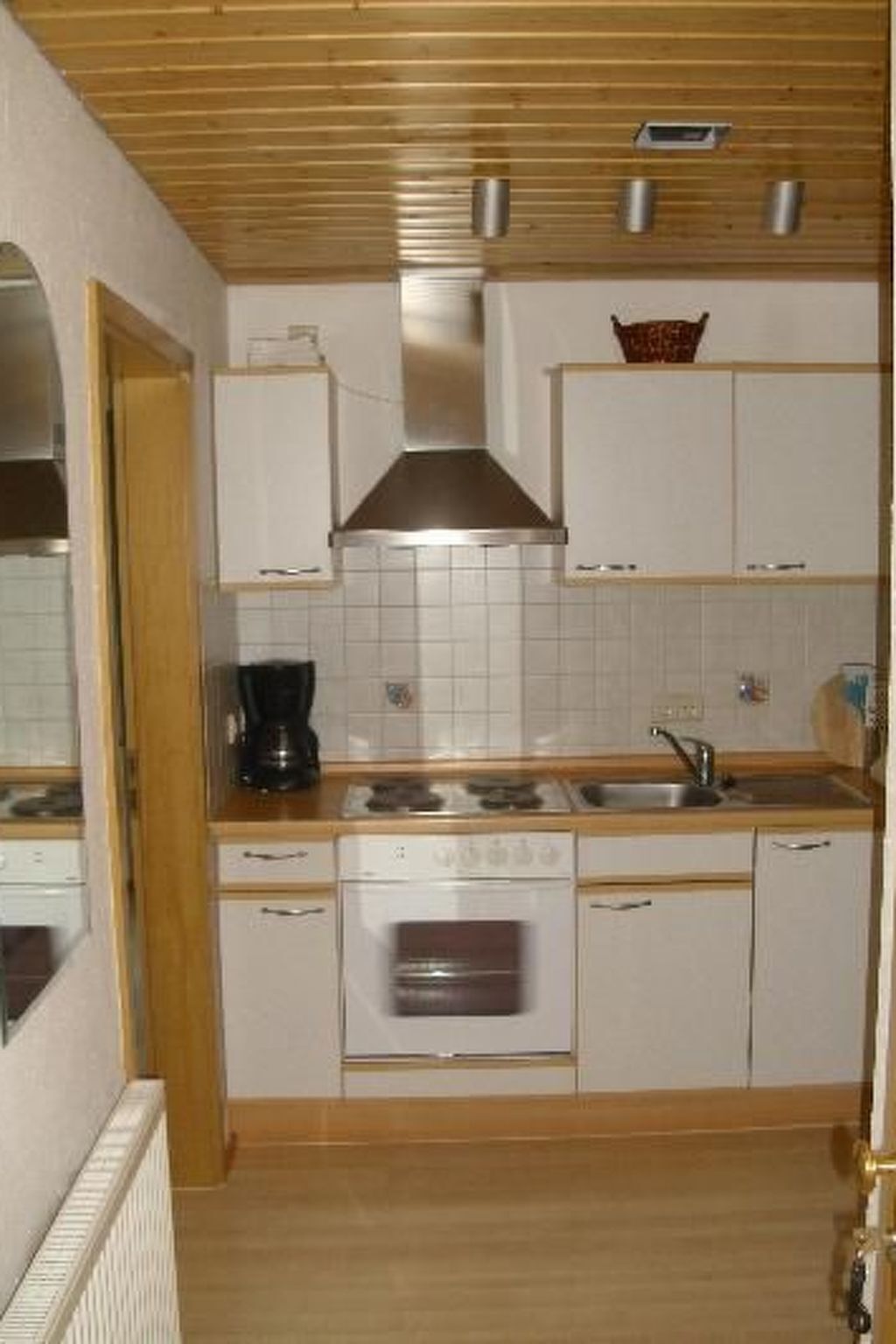 Une cuisine de taille réduite, avec des meubles blancs, une cuisinière, un évier et une machine à café.