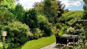 Eine Gartenlaube mit Tisch und Stühlen, umgeben von üppigem Grün und verschiedenen Pflanzen.