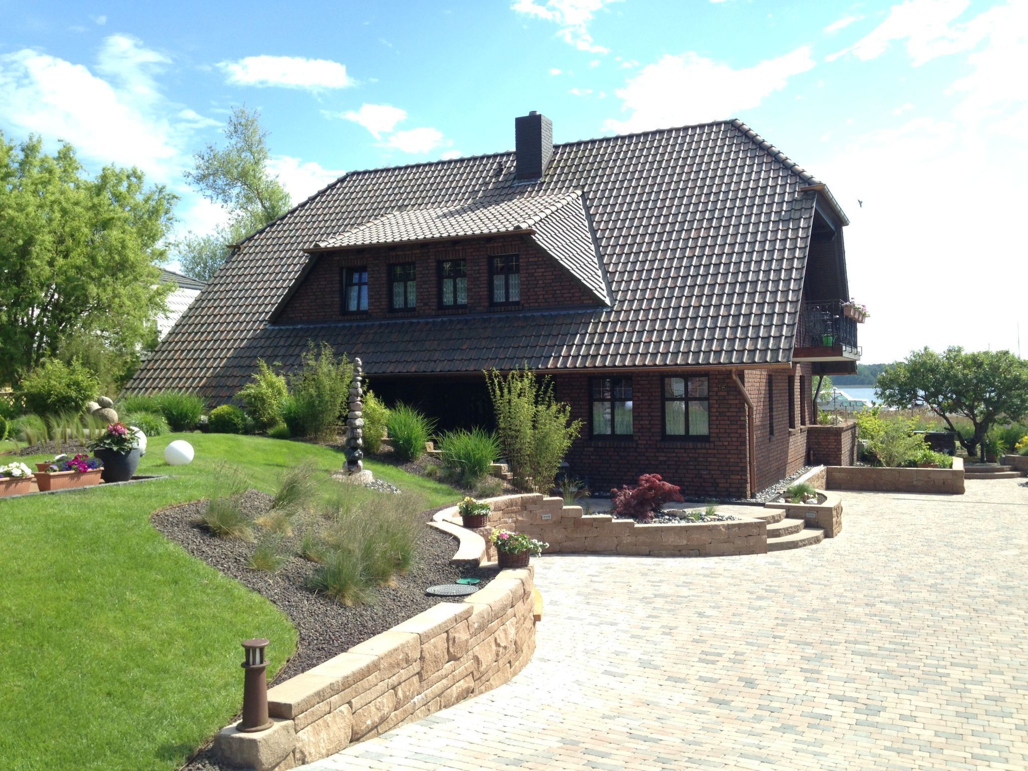 A two-story house with a sloped roof, brick exterior, and a landscaped front yard with a stone sculpture and various plants.