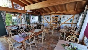 Un espacio de comedor al aire libre con mesas de madera y sillas de mimbre, rodeado por un techo y paredes rústicas de madera decoradas con varios adornos.