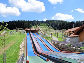 Eine Wasserrutsche mit mehreren Bahnen, umgeben von einem Holzzaun, und ein Holzgebäude im Hintergrund.