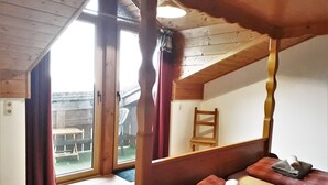 Una habitació de fusta amb sostre inclinat, un llit amb un coixí i una tovallola enrotllada, i una cadira.