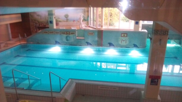 Una piscina coperta con acqua cristallina, un trampolino e un pavimento piastrellato.