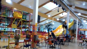 Area giochi al coperto con scivolo, strutture per arrampicata e tavoli e sedie per gli adulti.