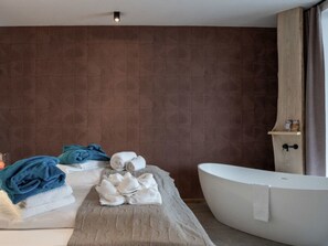 Ein modernes Badezimmer mit freistehender Badewanne, einem Handtuchhalter mit Handtüchern und einem Holzregal mit Pflegeprodukten.