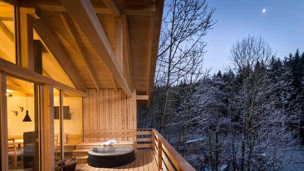 A wooden deck with a hot tub, glass doors, and a view of a snowy forest. - Oheblick by Interhome (Regen)