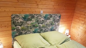 A wooden cabin room with a bed, a nightstand, and a wall with a leaf-patterned headboard. - in Atzenhain mit Großer Terrasse by Interhome (Atzenhain)