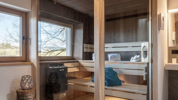 Uma sala de sauna com bancos de madeira, aquecedor e janela com vista para o exterior.