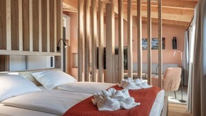 Quarto de hotel com duas camas, vigas de madeira, manta vermelha e vista do interior do aposento.