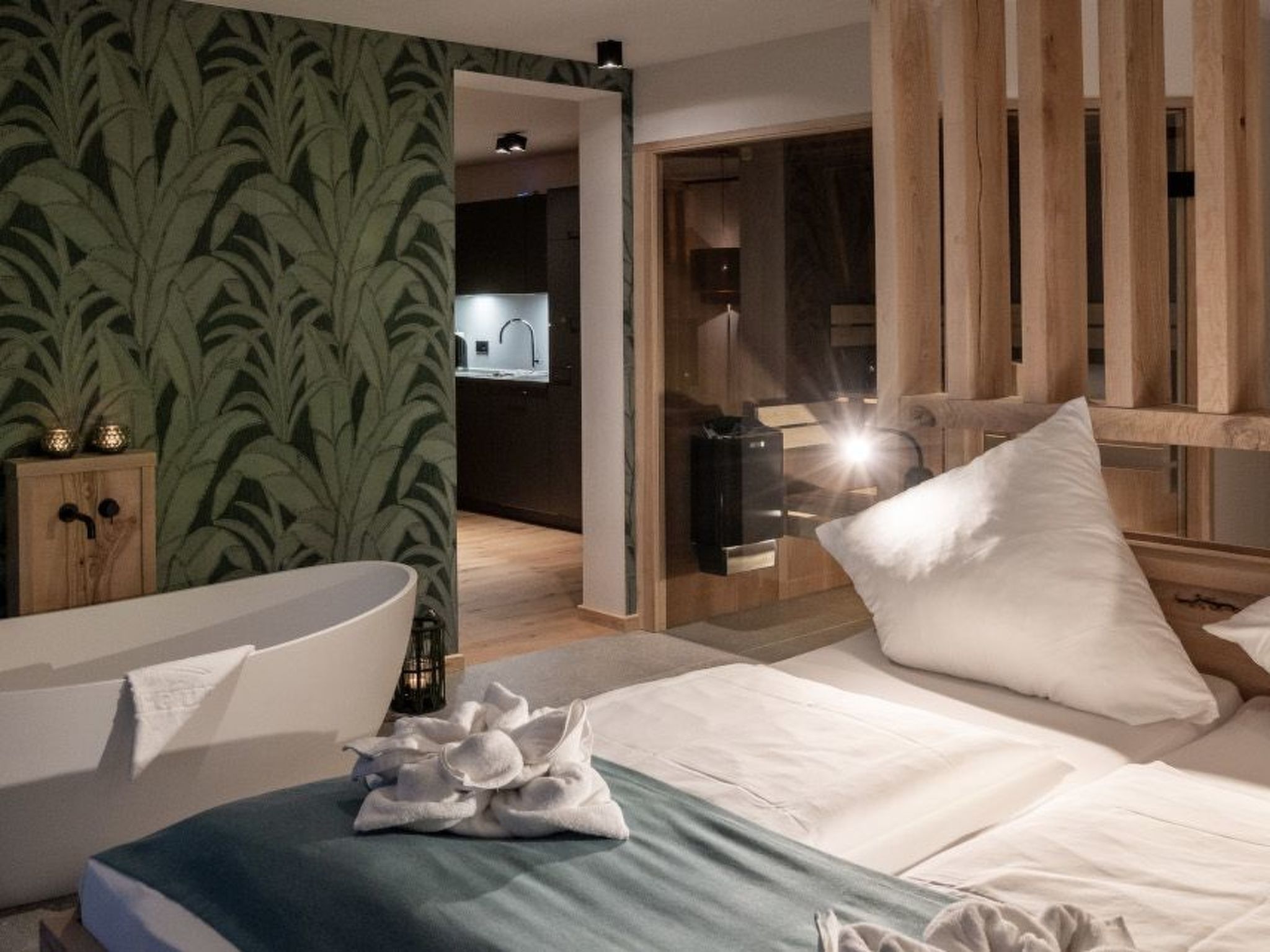 Une chambre d’hôtel moderne, avec un lit, une tête de lit en bois, une table de chevet et un papier peint à motifs verts.